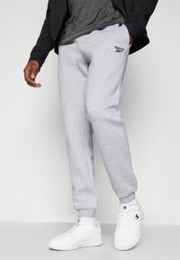 Pelēki sporta bikses, kas izgatavotas no kokvilnas maisījuma, ar elastīgu jostu, šauru kāju dizainu un Reebok logo kreisajā augšstilbā. Valkātas ar baltām kedām.