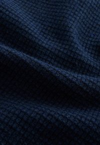 Strukturierter navyfarbener Stoff mit einem Rautenmuster, der eine weiche, gewebte Textur aufweist. Das Material wirkt gemütlich und ist schwer in der Haptik.