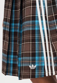 Καρό φούστα σε καφέ και μπλε χρώμα με λευκές ρίγες, από υφή ύφασμα, με κεντημένο λευκό λογότυπο στο στρίφωμα.