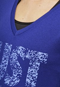 Blauw v-hals t-shirt gemaakt van een zachte stof, met een gestructureerde print in lichtblauw met een gepixeld patroon, gelaagd over een zwarte tanktop.