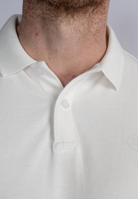 Bílá polokošile vyrobená z texturované bavlněné směsi, s žebrovaným límcem, dvouknoflíkovým zapínáním a decentním logem na hrudi.