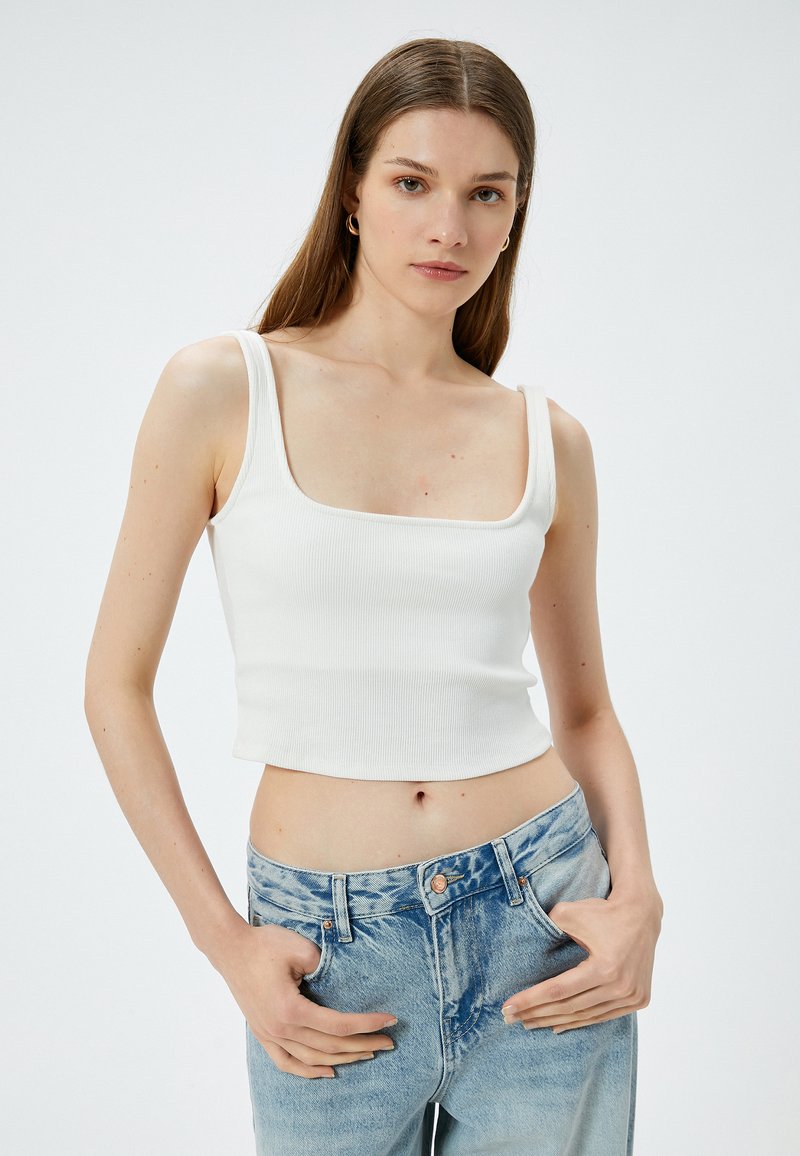 Witte geribbelde crop top met vierkante halslijn, gecombineerd met lichtblauwe high-waisted jeans. Huidige textuur, getailleerde silhoët, minimalistisch ontwerp.