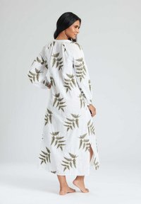 Vestido maxi blanco confeccionado en una tela ligera, con un estampado de helechos verdes por toda la prenda, mangas largas y aberturas laterales para facilitar el movimiento.