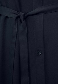 Mörkblå klänning med ett tygbälte, enknappsstängning och jämn textur med vertikala sömnadsdetaljer.