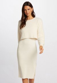 Gekropte, fluffy trui in off-white met lange mouwen. Bijpassende ribgebreide rok tot de knie met een zijsplit. Eenvoudig ontwerp en textuur.