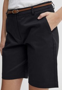 Shorts noirs avec une texture lisse, dotés de poches latérales et d'une ceinture marron. Le design est ajusté avec une coupe décontractée et des lignes épurées.