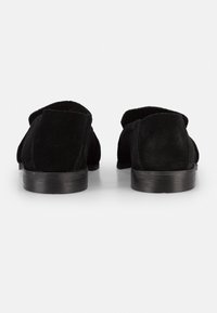 Mocassini neri in suede con suola in pelle liscia, punta arrotondata e design minimalista. La parte posteriore presenta una linea superiore morbida e non strutturata.