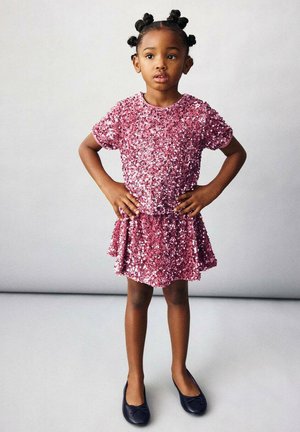 Robe rose en sequins avec manches courtes et jupe évasée, associée à des ballerines noires. La robe est ornée de sequins scintillants pour une texture brillante.