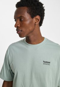 Ljusgrön t-shirt gjord av mjukt tyg, med korta ärmar och rundad halsringning. Liten svart logotyp på vänster bröstområde.