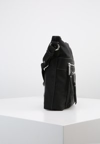 Borsa a tracolla nera in pelle con tasca anteriore con zipper e tracolla regolabile, posizionata in verticale su un piedistallo bianco contro uno sfondo neutro.