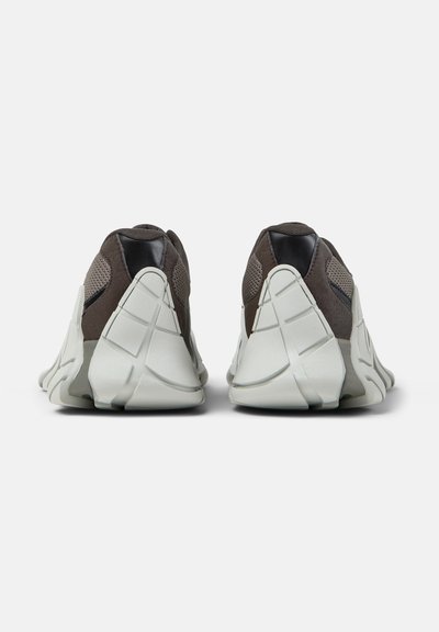 Paire de chaussures de sport modernes grises et noires avec des semelles blanches épaisses et uniques en leur genre, vues de dos sur un fond blanc.