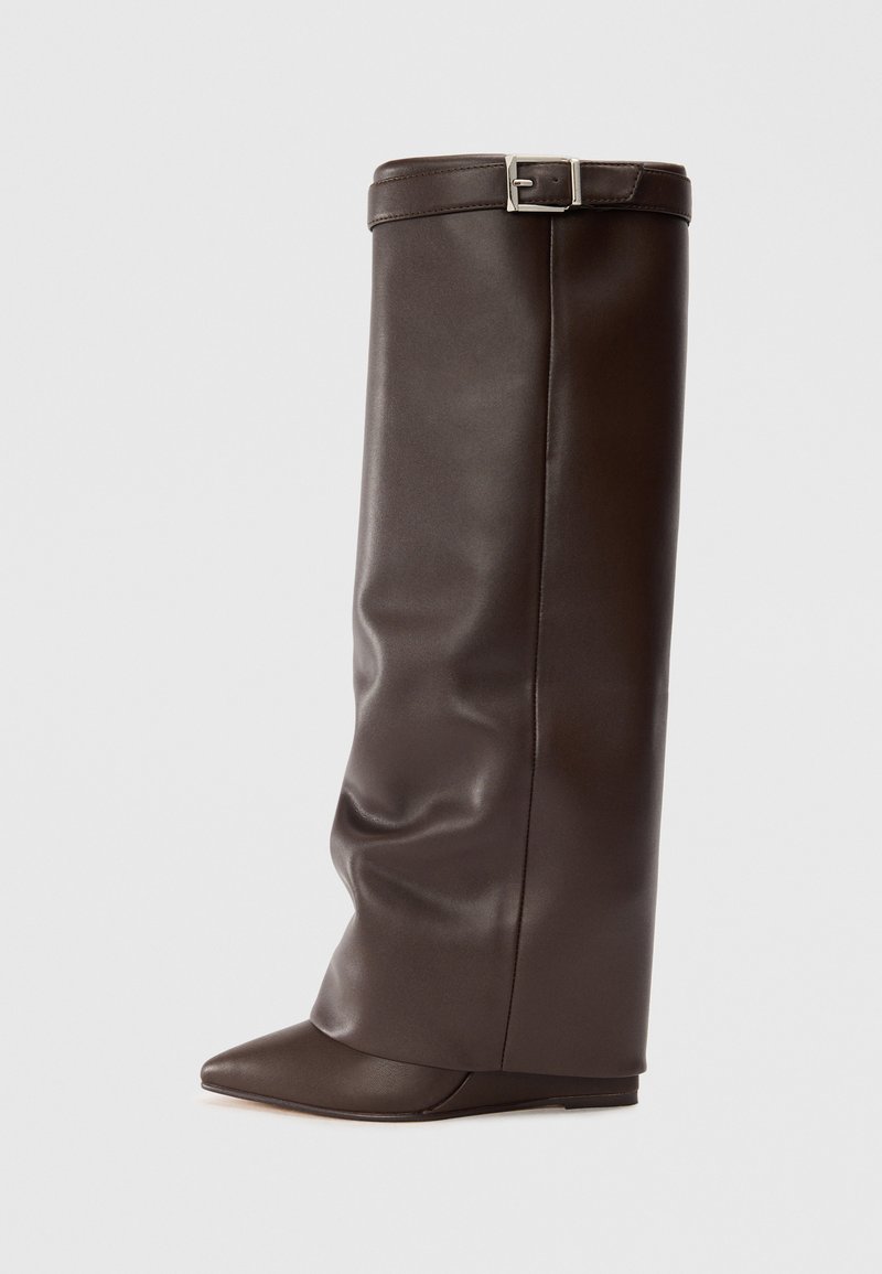 Bottines en cuir marron, hauteur genou, au design décontracté, avec un bout pointu et un talon plat. Présente un accent de boucle en haut. Texture lisse.