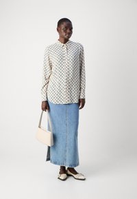Long-sleeve shirt in cream with blue diamond pattern, paired with a light denim maxi skirt. Features a white handbag and cream shoes.