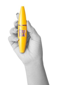 Gul mascara-tub med en avsmalnande design och lila text, hålls i en hand mot en vit bakgrund. Slät, blank yta.