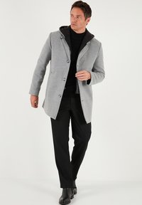 Šedý kabát z vlněné směsi s kapucí, jednobrečňový střih a knoflíky, ve spojení s černými kalhotami a koženými botami. Hladká textura.