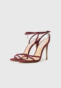 Red suede high-heeled sandals with glittery cross straps and ankle buckle. Features a smooth beige insole and slim stiletto heel.