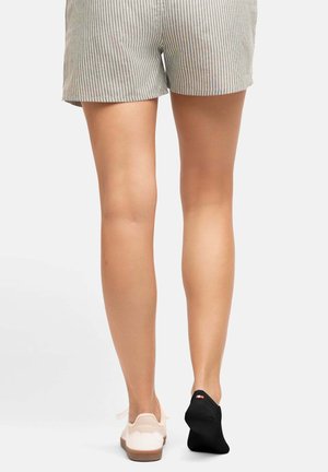 Pantalones cortos de tela a rayas, gris claro con rayas oscuras; lleva una zapatilla blanca con suela texturizada y un calcetín invisible negro con un logotipo.