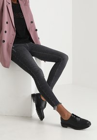 Czarne, obcisłe jeansy z wysokim stanem i postrzępionym wykończeniem, połączone z czarnym topem i szarym żakietem, uzupełnione czarnymi butami na sznurówki.