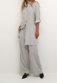 Dwuczęściowy strój w paski składający się z koszuli z guzikami i spodni o szerokich nogawkach w kolorze białym i czarnym, wykonany z lekkiego materiału; eleganckie czarne buty.