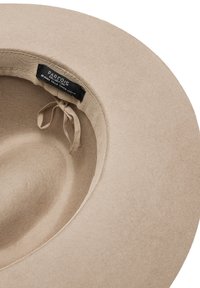 Beżowy filcowy kapelusz o szerokim rondzie i gładkiej fakturze. Wewnątrz znajduje się materiałowa opaska z metką oraz małym regulowanym wiązaniem.