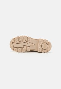Beige gummi såle med et teksturert, sikksakkmønster og hevede trekantede aksenter. Kjennetegnes av et sirkulært logoavtrykk nær hælen.