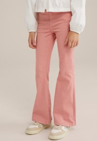 Rosa utsvängda jeans i denim, med en åtsittande midja och lätt stretch, i kombination med vita och beige sneakers.