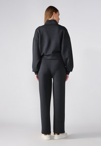 Black sweatshirt and matching pants in a smooth fabric, featuring oversized sleeves and a relaxed fit, paired with white sneakers.