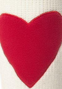Rode hartaccent op zacht wit textiel met een geribbelde textuur. Het hart heeft een gestikte rand, wat een gelaagde uitstraling creëert.