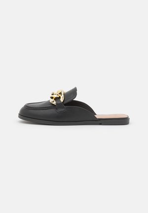 Sort læder slip-on mule med lav, flad sål og stor guldkæde-detalje hen over toppen.