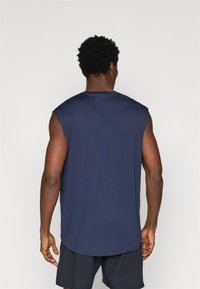 Mornarsko brezrokavno športno majico s krožnim izrezom, izdelano iz lahkega materiala, s rahlo ukrivljenim robom in gladko teksturo.