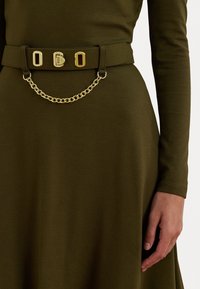 Olivově zelený látkový pásek s třemi zlatými obdélníkovými sponami a dekorativním zlatým řetízkem. Nesený přes ladící šaty.