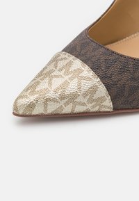 Chaussure plate à bout pointu avec corps texturé marron foncé et bout beige à motif, sur fond blanc uni.