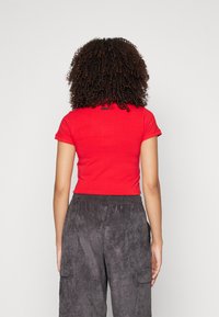 Czerwony krótki T-shirt z krótkimi rękawami i detalem logo na plecach, zestawiony z szarymi, teksturowanymi spodenkami typu cargo z elastycznym pasem.