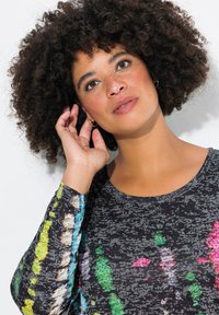 T-shirt à manches longues multicolore avec une base noire ornée de motifs abstraits vibrants en vert, rose et bleu, agrémentée de petites applications en métal.