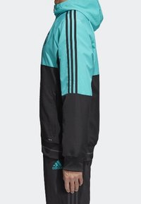 Teal en zwarte sportjack met een capuchon, voorzien van drie zwarte strepen op de mouwen en ritszakken. Soepele textuur, atletisch ontwerp.