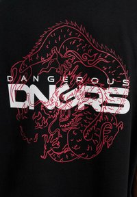 Svart T-skjorte med et rødt dragegrafikk som er sammenflettet med fett hvit tekst som sier "DANGEROUS DNGRS." Jevn tekstur og standard passform.