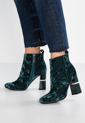 Bottines en velours vert avec un haut bloc talon, dotées d'une fermeture éclair sur le côté, d'une surface texturée et d'un accent rayé contrastant sur le talon.