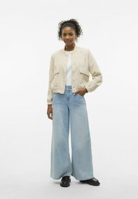 Krēmveida kordūra bomber jakas ar divām priekšējām kabatām, kombinēta ar gaiši ziliem plaša piegriezuma džinsiem un melnām platformas kurpēm. Vienkāršs, strukturēts dizains.