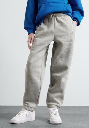 Graue Sweatpants mit elastischen Bündchen und einem Kordelzugbund, kombiniert mit weißen Sneakers. Der Stoff ist weich und hat eine dezente Textur.