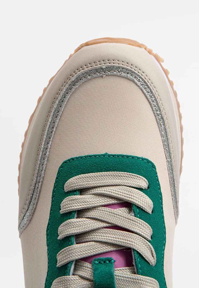 Beige Sneaker mit grünen Akzenten, strukturiertem Canvas-Obermaterial, grauer Naht und Gummisohle. Die Schnürsenkel sind hellgrau mit einer pinken Zunge.