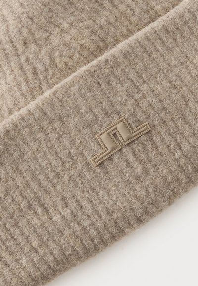Gros plan sur un tissu tricoté beige avec un petit emblème rectangulaire présentant un motif géométrique en relief.
