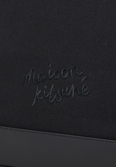 Bolsa de lienzo negra con el nombre de la marca "maison kitsuné" en relieve en un tono a juego, y un acento de piel negra suave en la parte inferior.