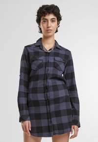 Abito camicia a maniche lunghe in una fantasia a quadri blu scuro e nero, con chiusura a bottoni, due tasche sul petto e una vestibilità morbida.