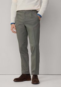 Svetlo šedo-zelené nohavice so slim fit strihom, so splošteným predkom, bočnými vreckami a hladkou textúrou. V páre s tmavohnedými topánkami.