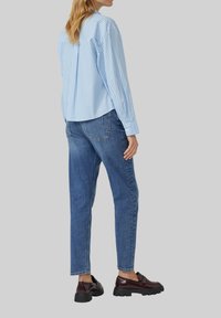Lichtblauw gestreept overhemd met knopen, blauwe spijkerbroek en bordeauxrode schoenen. Het overhemd heeft lange mouwen en een relaxte pasvorm; de spijkerbroek is tapered met een klassieke stijl.