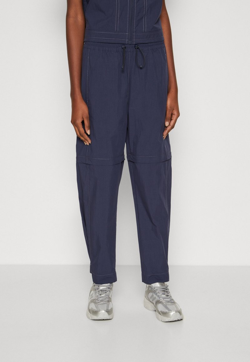Marineblauwe cargo broek met elastische tailleband en trekkoord. Voorzien van met een rits afgesloten zakken, contrasterende stiksels en een losse, taps toelopende pasvorm.