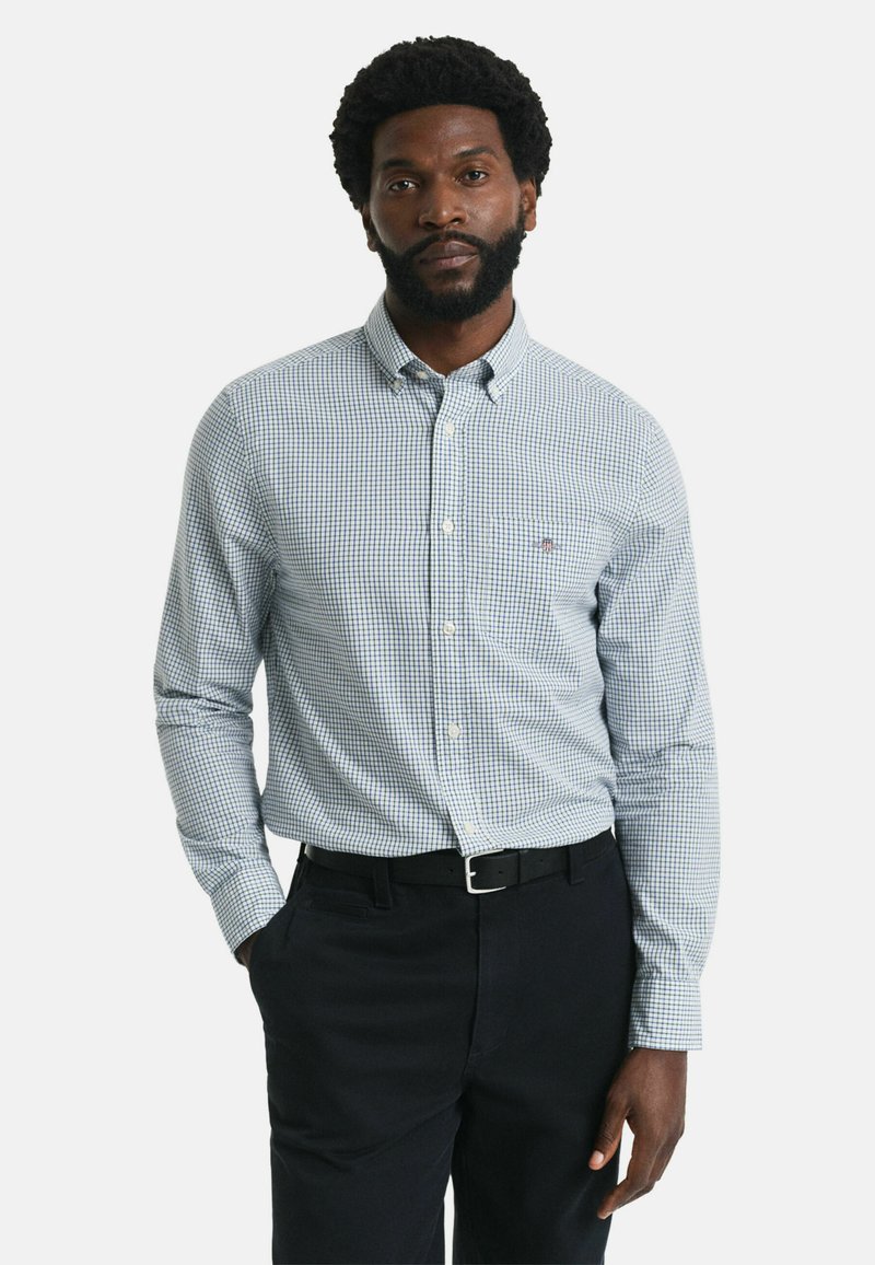 Blauw en wit geblokt overhemd met lange mouwen en een knoopsluiting kraag, gecombineerd met donkere broek. Heeft een klein logo op de borst.