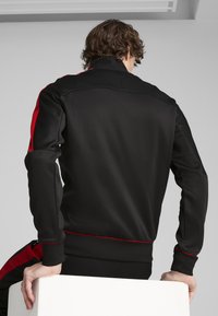 Zwarte trainingsjack met rode accenten, met een hoge kraag en elastische manchetten. Gemaakt van glad materiaal met een aansluitend ontwerp.