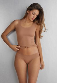 Nude naadloze tanktop en bijpassende slips gemaakt van zacht materiaal, met een aansluitend ontwerp en een gladde textuur.