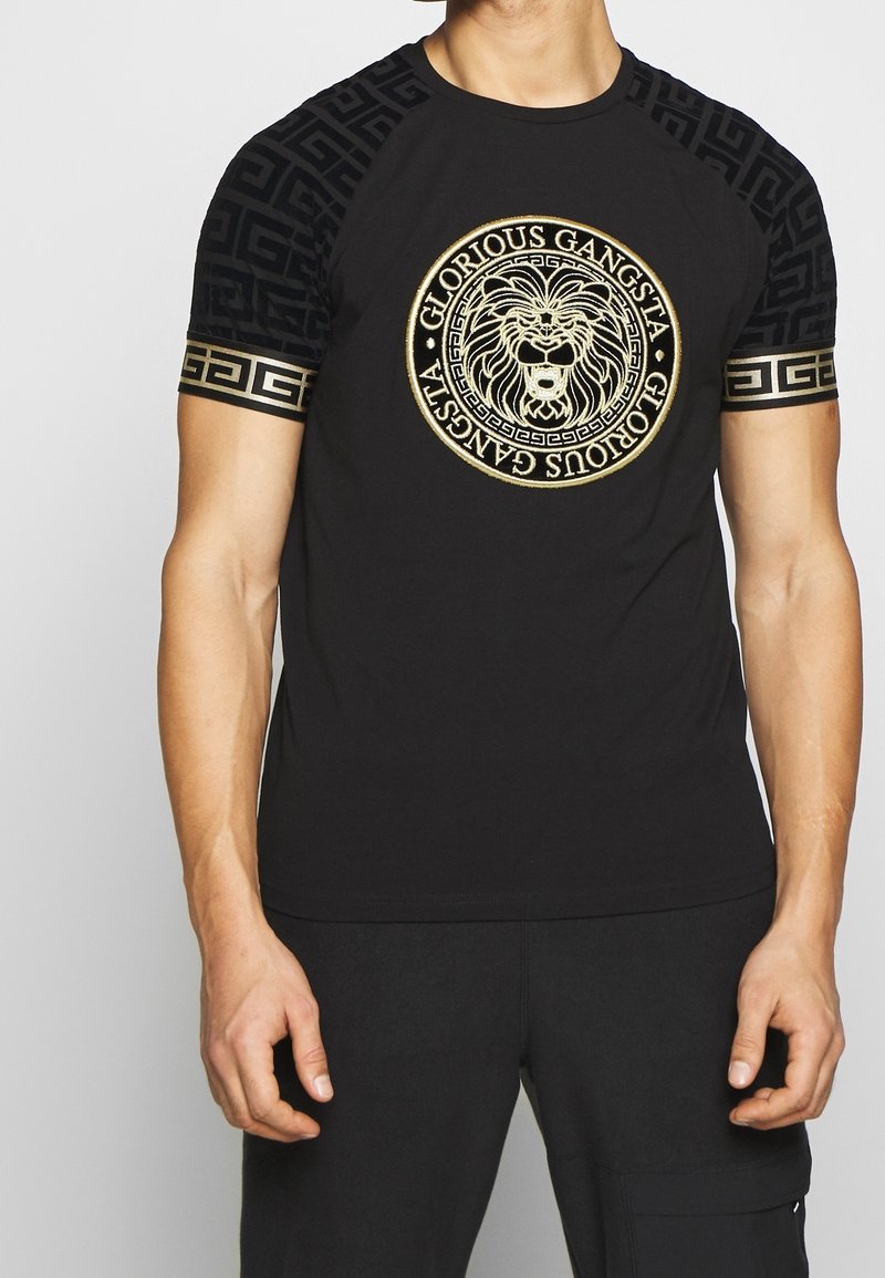 Camiseta negra de manga corta, con un gráfico circular de león dorado y patrones intrincados en negro y dorado en las mangas.